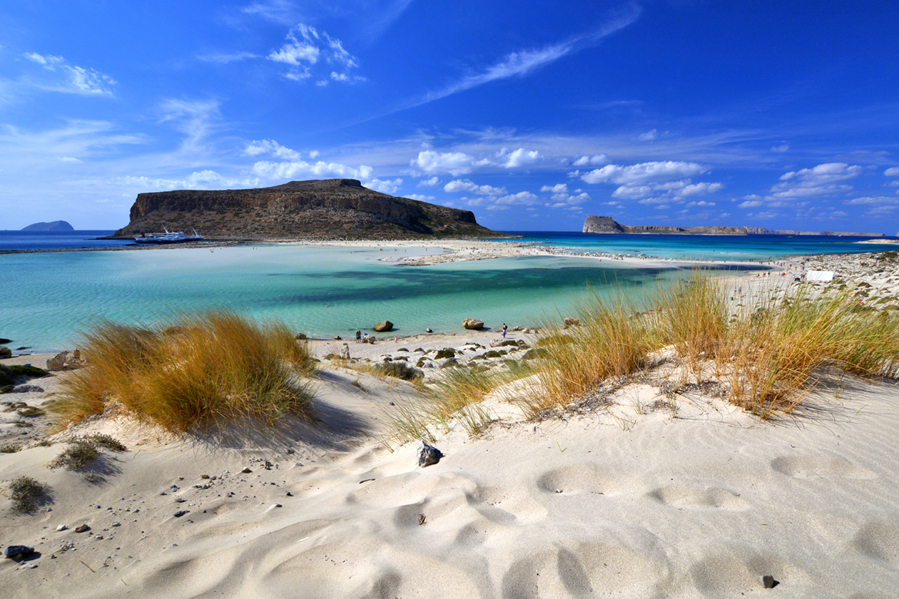 Scenic view of Balos Lagoon in Crete, Greece, showcasing turquoise waters, sandy dunes, and a bright blue sky.
