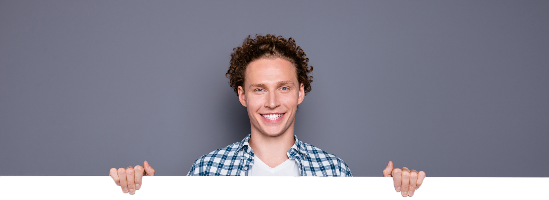 Man smiling confidently while holding a blank banner against a gray background, symbolizing friendliness and approachability.