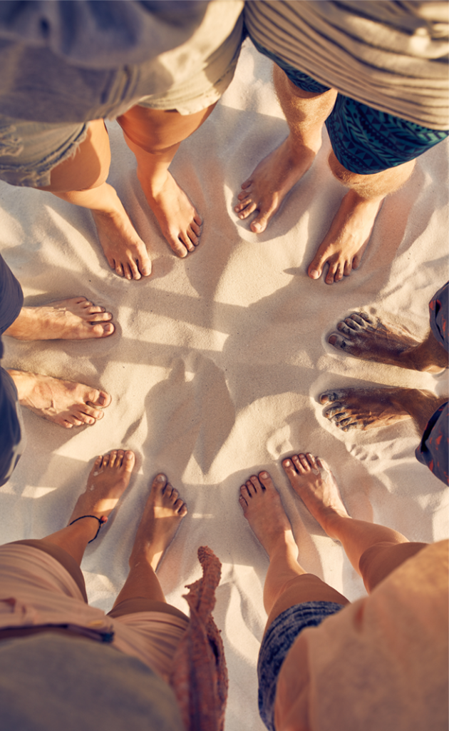 MMiddleChania3Sep11 Group of friends standing barefoot in a circle on a sandy beach, showing togetherness and summer vibes.
