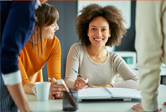 Team of professionals engaged in a discussion around a table, with a smiling woman in the center.
