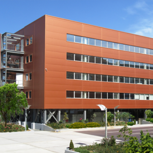 Contemporary TP office building with a sleek red facade and large windows, surrounded by greenery under a clear blue sky.