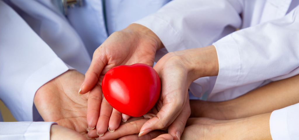 Close-up of hands gently holding a red heart-shaped object, symbolizing care and compassion.