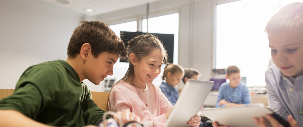 education Group of children in a classroom working together on tablets and digital devices, smiling and collaborating.