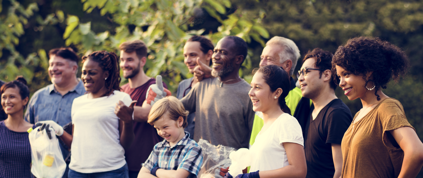 Diverse group of volunteers of different ages standing together outdoors, smiling after a community activity.