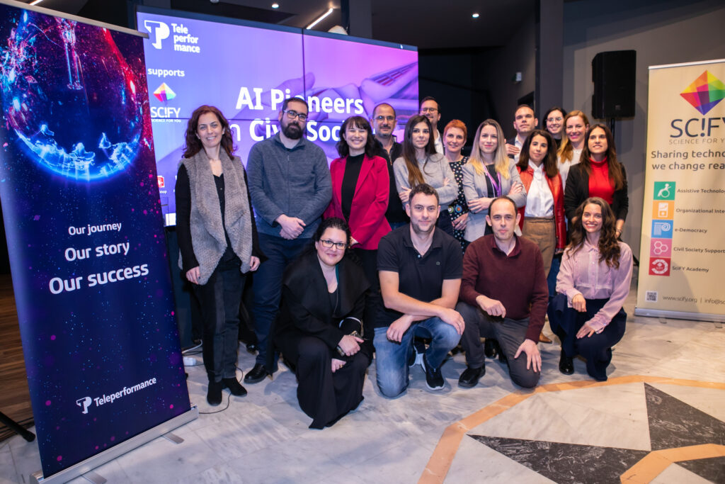 Group photo of TP Greece employees and SciFY representatives during the “AI Pioneers in Civil Society” collaboration event. Participants are standing and smiling in front of banners from Teleperformance and SciFY promoting technology for social impact.