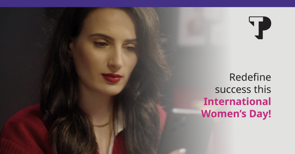 Woman with long dark hair and red lipstick looking at a tablet, with text reading “Redefine success this International Women’s Day!” and the TP logo.
