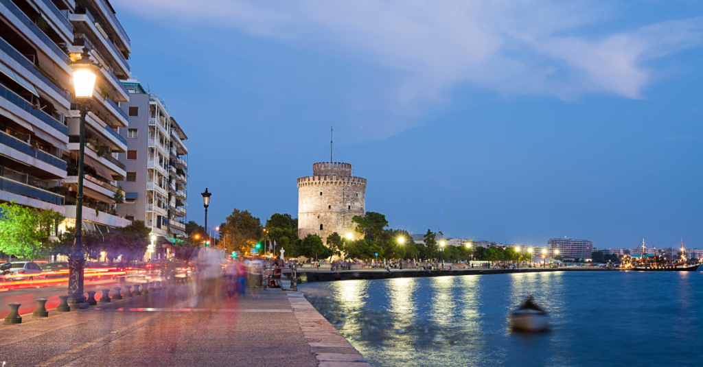 Evening view of the Thessaloniki waterfront, featuring the White Tower and reflections of city lights on the water.