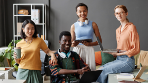 A diverse team of colleagues in a modern workspace, smiling and holding laptops and tablets, promoting inclusion and teamwork.