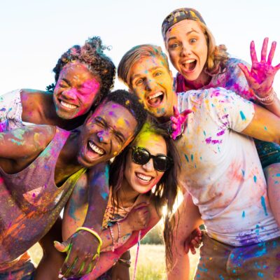 happy young multiethnic friends with colorful paint on clothes having fun together at holi festival