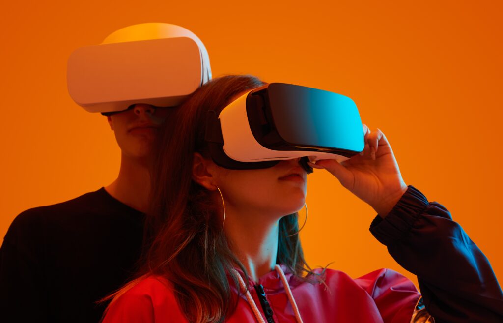 Two people wearing virtual reality headsets against an orange background, exploring immersive digital experiences.