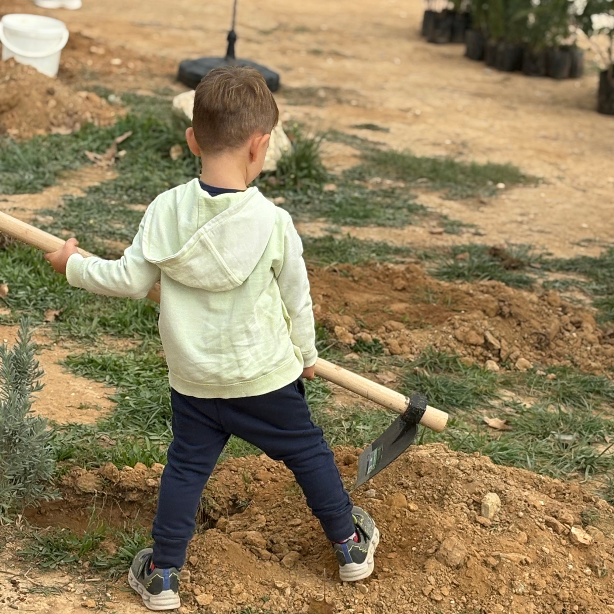 A young child holding a small shovel and digging into the soil during a community tree-planting activity.