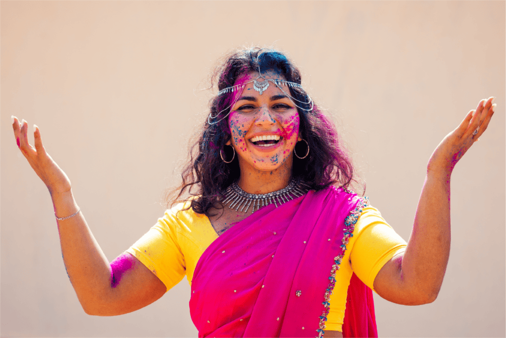 A woman celebrating Holi, wearing a bright sari and covered in colorful powder, smiling joyfully.