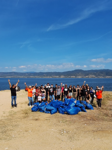 A group of TP people posing together after a beach cleanup, with bags of collected waste in front of them and the sea and mountains in the background.